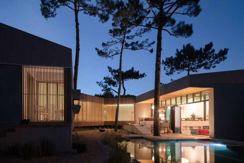 Night view of courtyard with illuminated timber screen and reflecting pool between two building volumes