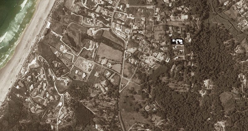 Aerial view showing scattered residential buildings among farmland and coastal vegetation near the shoreline