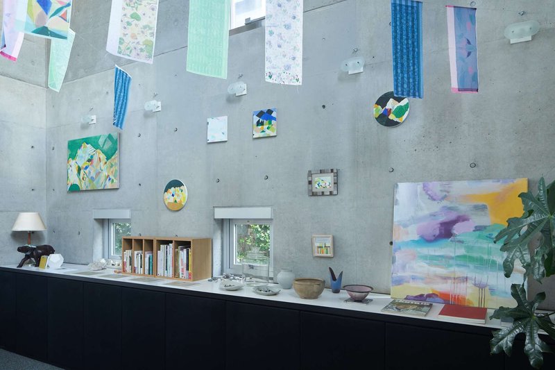 Board-formed concrete wall displaying paintings and artworks above black counter with potted plant