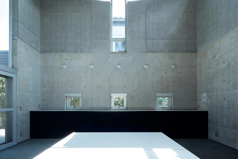 Concrete walls with small punched windows and a black horizontal band above the white floor