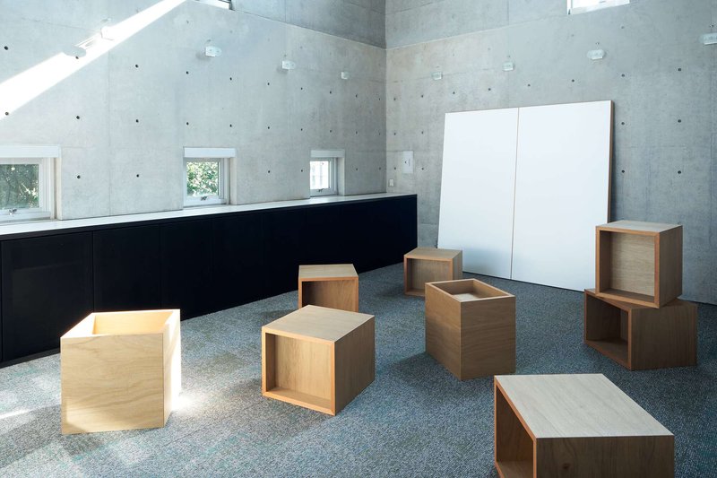 Interior room with scattered wooden cube furniture and a white panel against exposed concrete walls