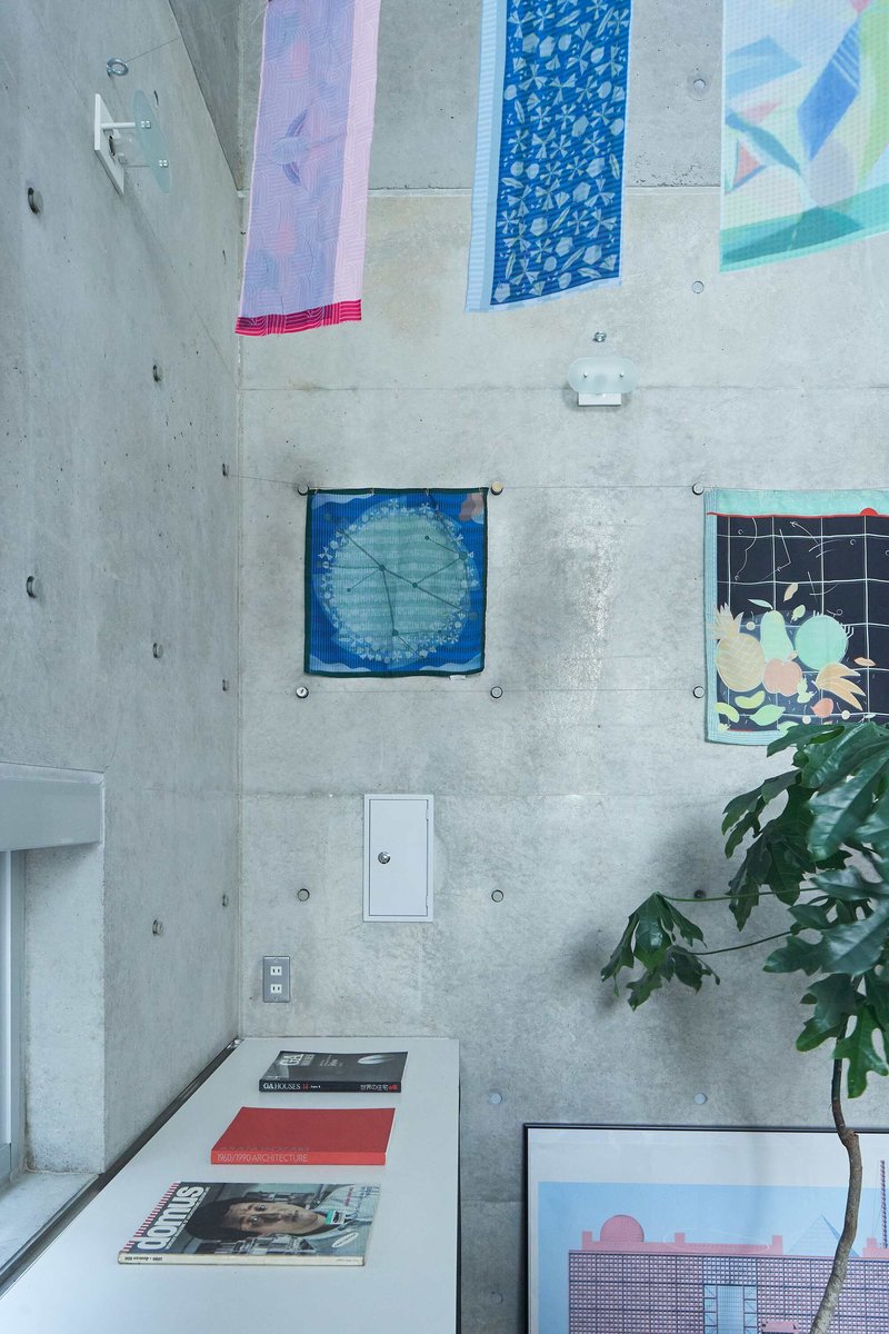 Overhead view of a white work surface with patterned fabric panels pinned to the concrete wall and a potted plant