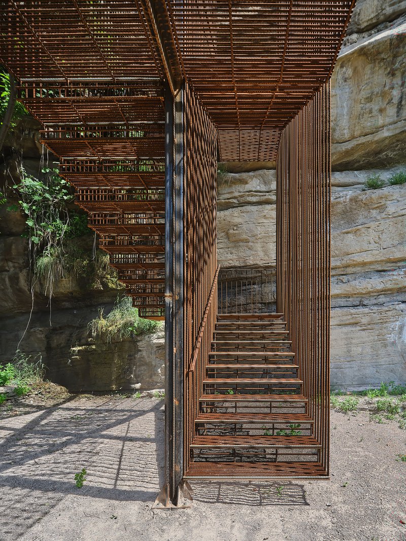 Looking up through the staircase core with weathered steel slats and exposed rock walls casting shadows