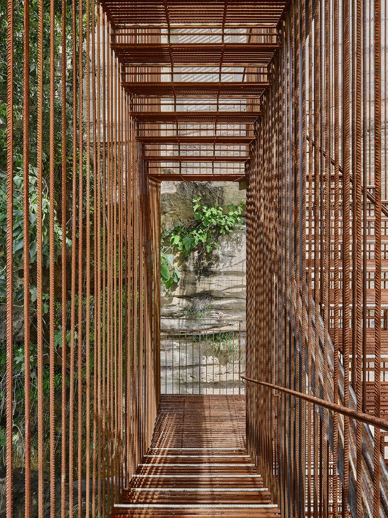 View through the narrow metal stair enclosure with rod balusters framing weathered stone and vegetation below