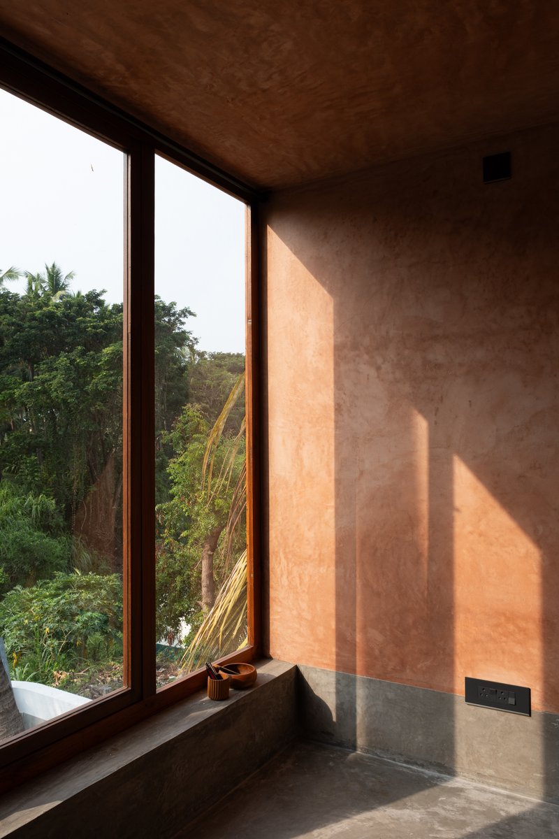 Corner window with timber frame casting afternoon light onto the pink plastered wall