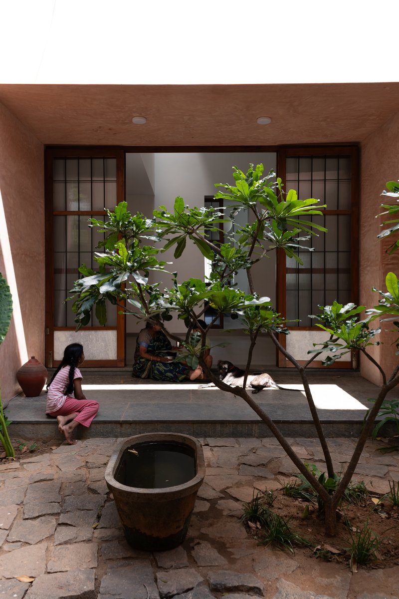 Courtyard with dark gridded sliding doors, ceramic pot, and frangipani tree under an earthen plaster ceiling