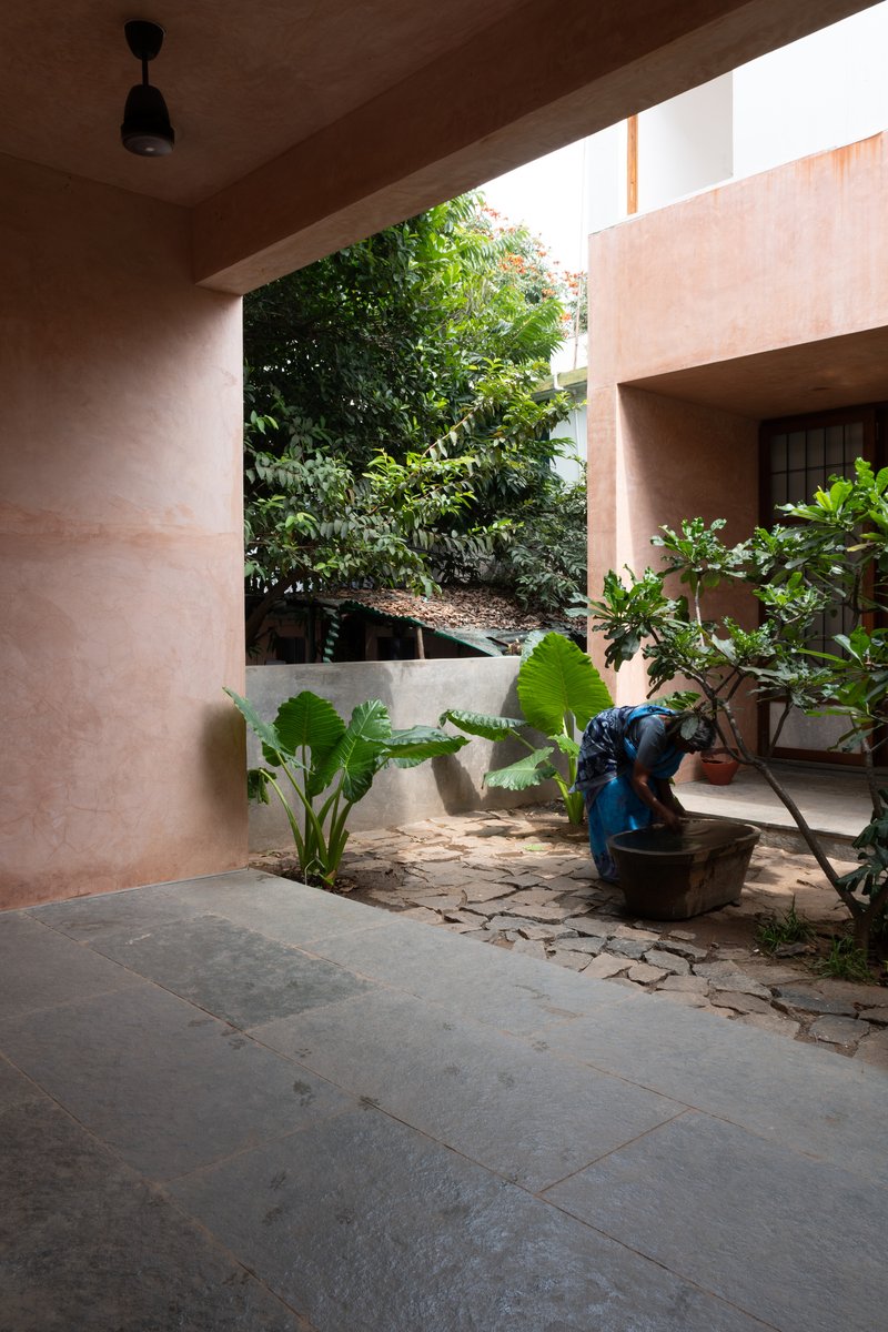 View through an earthen plaster portal toward a planted garden with areca palms and stone paving