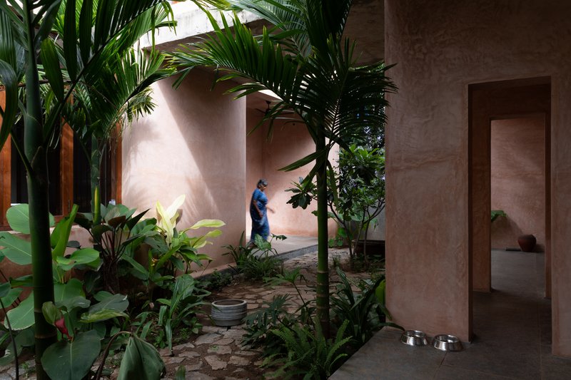 Garden passage at dusk with tropical planting, earthen plaster archway, and a figure walking through shadow