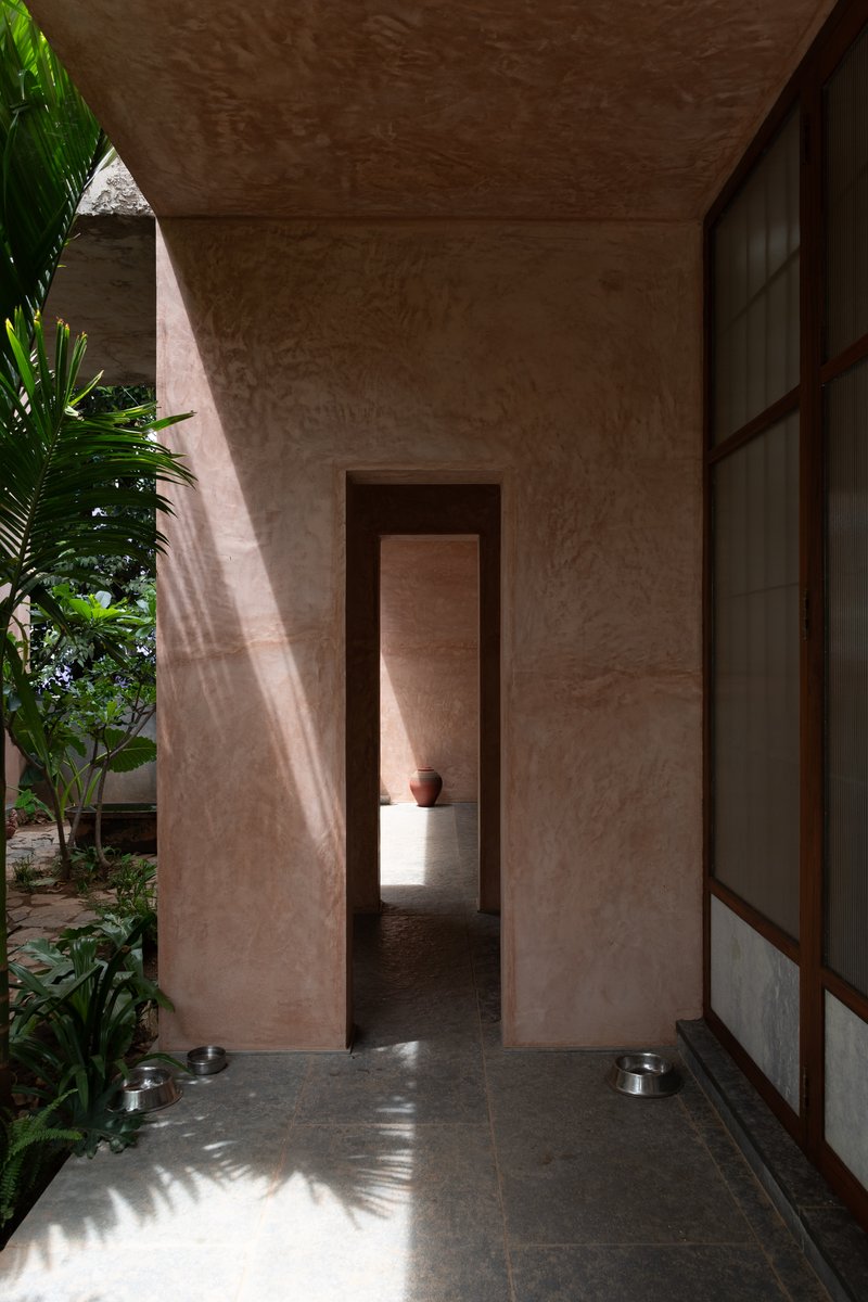 Covered walkway with framed doorway opening and gridded screen wall casting palm shadows in morning light