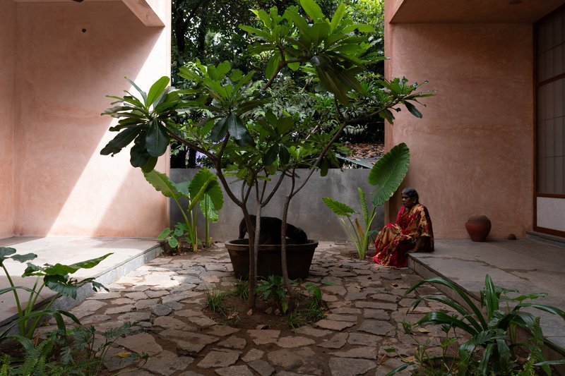 Courtyard with stone paving and central tree sheltered by pink rendered walls with a seated figure