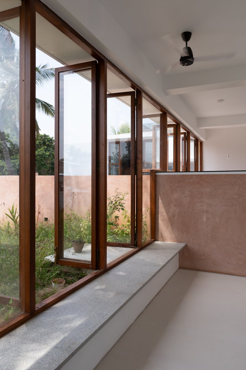 Row of timber-framed glazed doors with stepped sill overlooking planted courtyard under diffuse sky