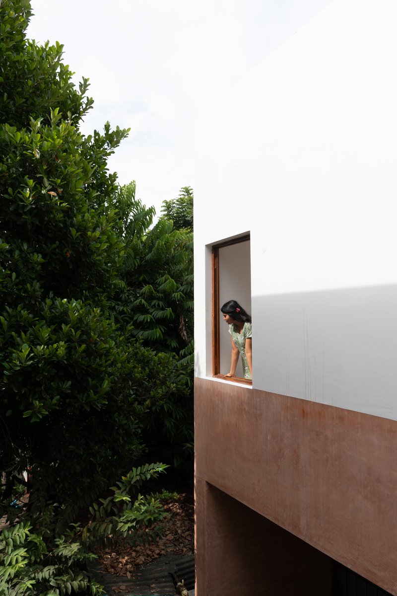 Cantilevered balcony with wood base and white parapet where a person stands beside foliage