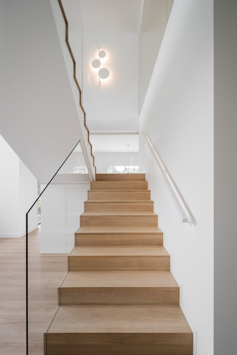Light timber staircase with thin steel handrail and white walls beneath a circular pendant fixture