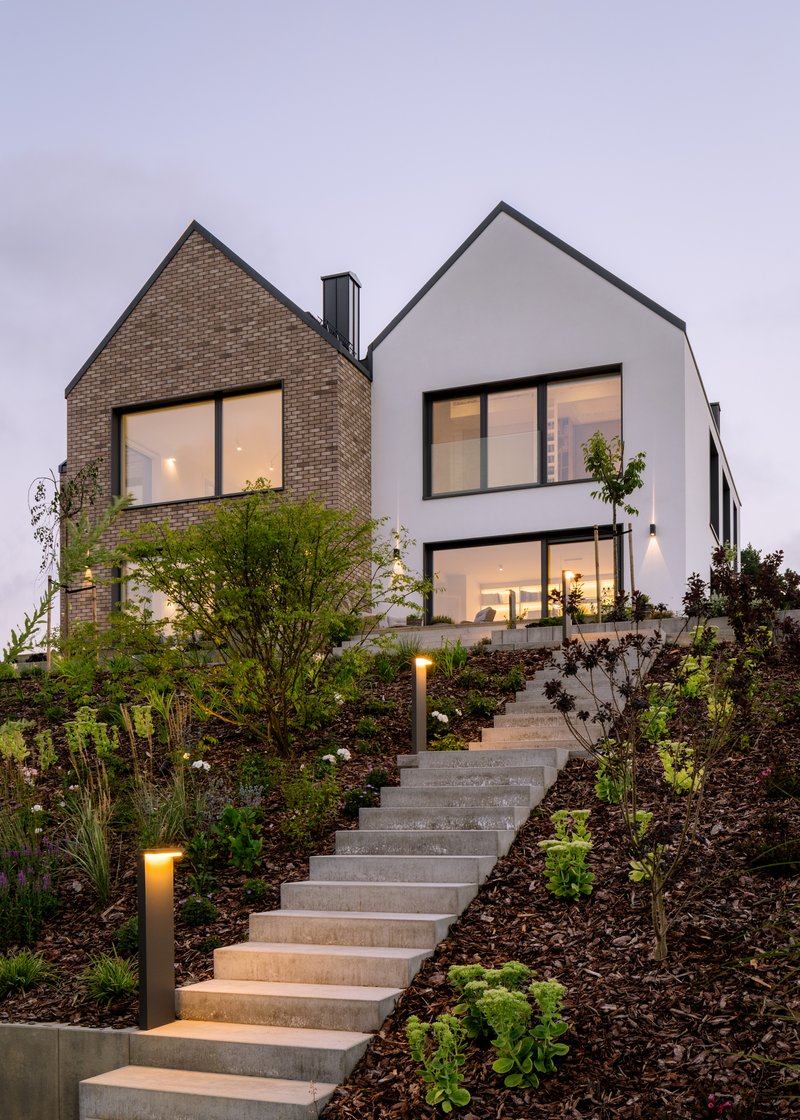 Two gabled volumes in white render and tan brick with landscaped steps at dusk