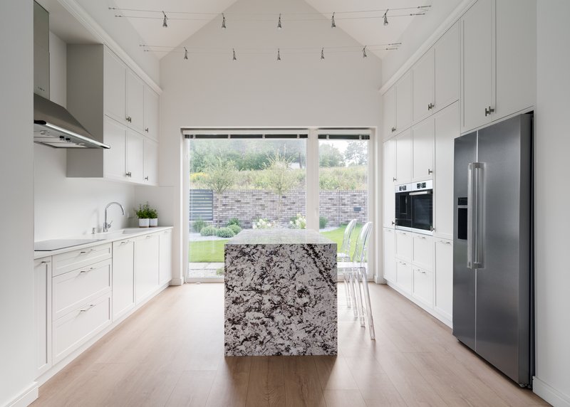 White galley kitchen with granite island, track lighting, and glass doors opening to the lawn beyond