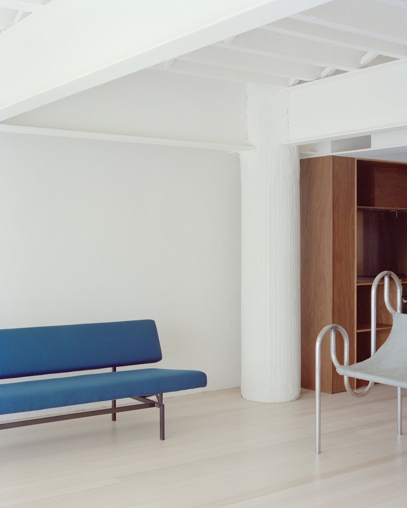 White room with exposed timber ceiling joists, blue upholstered sofa and cylindrical painted column