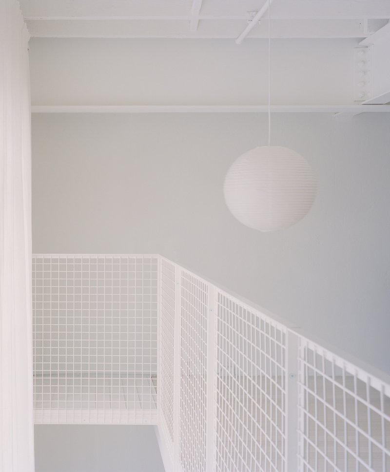Upper level passage with white wire mesh railing and spherical pendant light under exposed joists