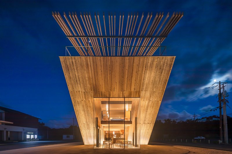 Illuminated timber pavilion with inverted pyramidal form and exposed rafter crown at blue hour