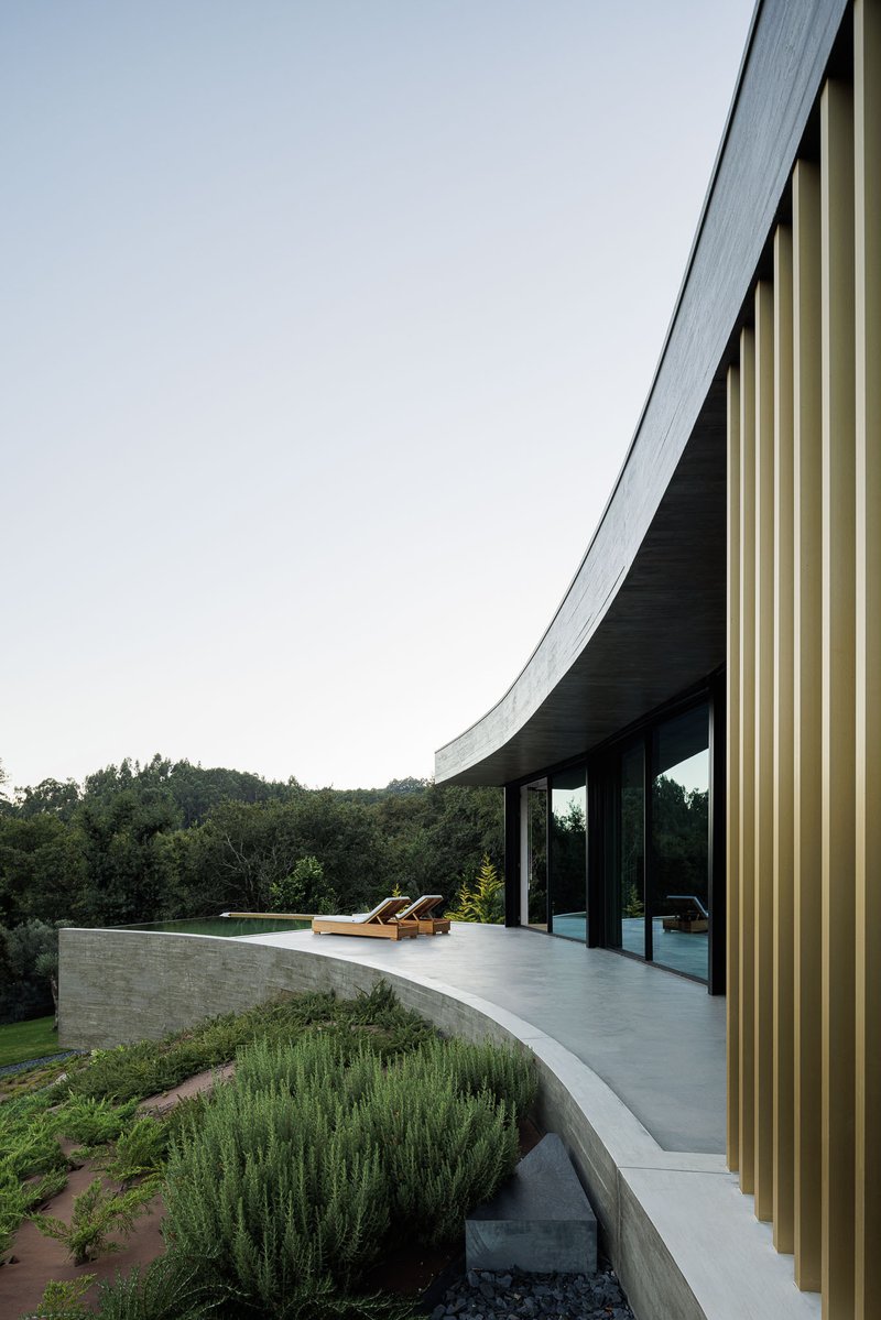 Terrace with pool and lounge chairs overlooking forested valley at twilight under the curved roof