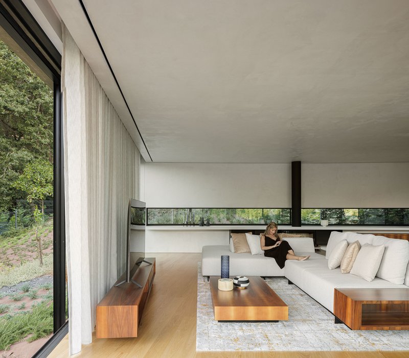 Living room with floor-to-ceiling glazing, sheer curtains, and a person seated on a low white sofa