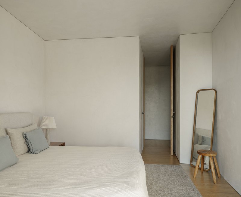 Bedroom with pale plaster walls and a narrow doorway leading to an adjacent corridor
