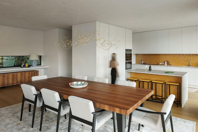 Dining area with a walnut table and white cabinetry with yellow tile backsplash in the kitchen