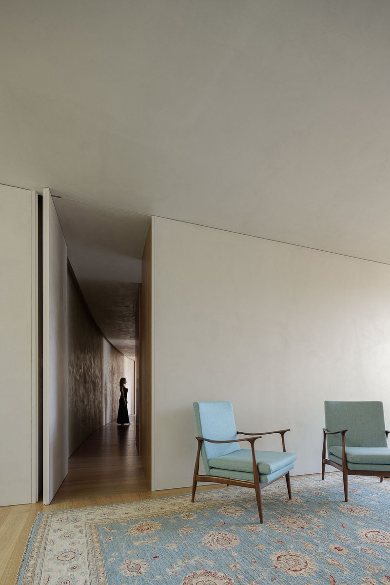 Living room with two midcentury armchairs and doorway opening to corridor where a figure walks