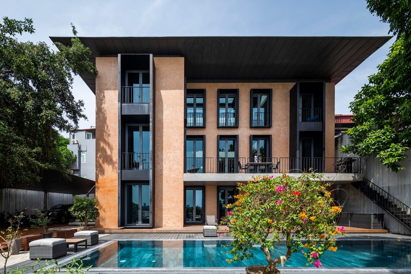 Rear facade with terracotta-textured panels overlooking a swimming pool framed by flowering trees