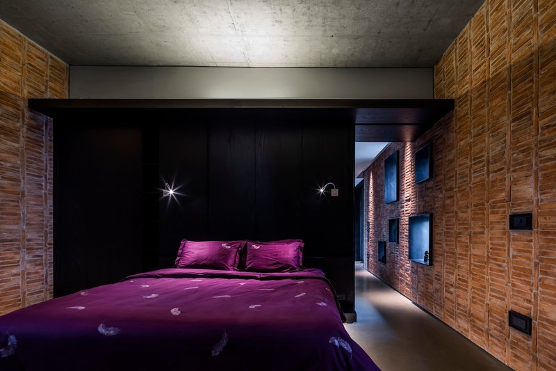 Bedroom with black millwork alcove and brick wall corridor under exposed concrete ceiling