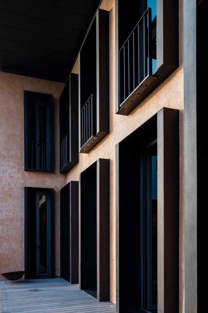 Facade detail showing deeply recessed window frames in textured plaster with metal railings and vertical louvers