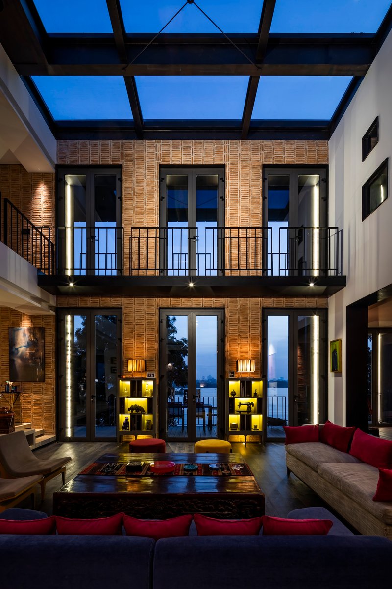 Double-height living room with brick walls, glass skylight and a mezzanine balcony at dusk
