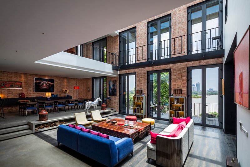 Double-height living room with mezzanine balcony and floor-to-ceiling glass doors opening to greenery