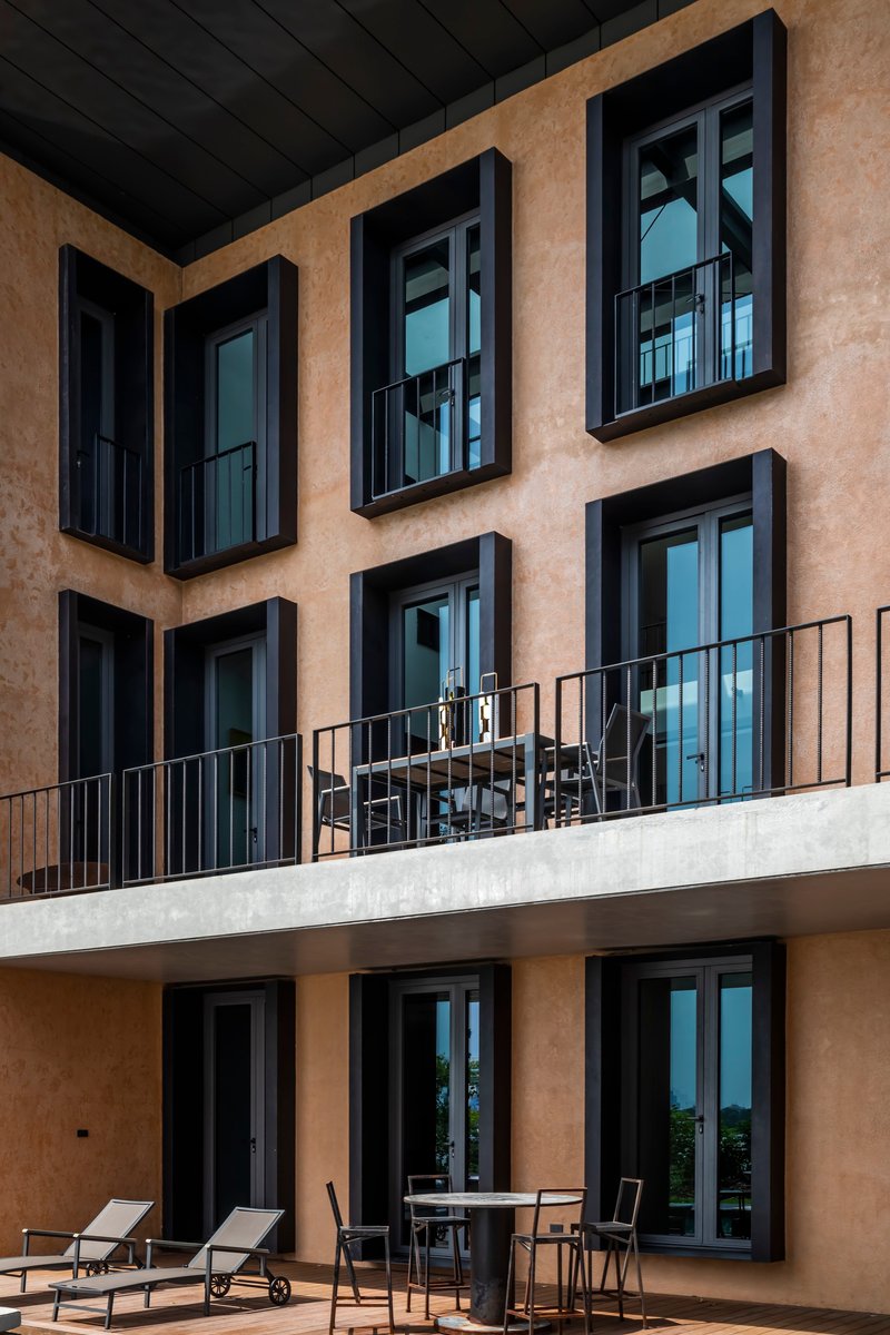 Facade detail showing black-framed windows on terracotta plaster with furnished concrete balcony terrace