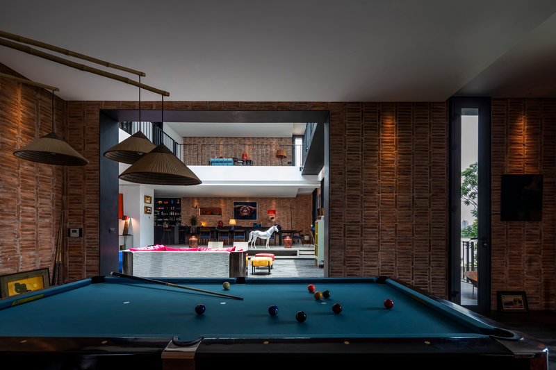 Pool table beneath pendant lights with layered timber slat walls and a double-height void beyond