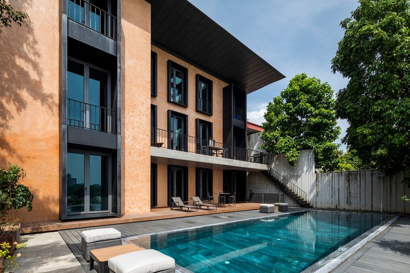Pool terrace with timber decking, concrete balconies and tree shadows on the terracotta facade