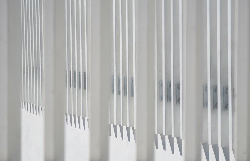 Close-up of white vertical slat screen with sharp shadow lines cast across its stepped profile