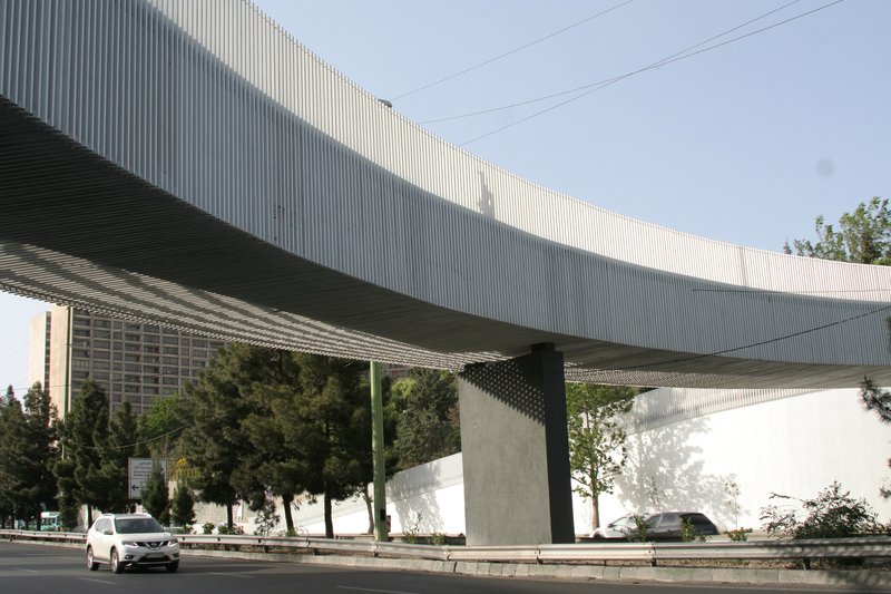 Underside of the bridge showing corrugated metal soffit and concrete support columns with passing vehicles below