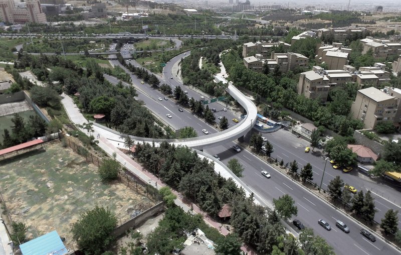 Aerial view of a curving pedestrian bridge crossing a multi-lane boulevard lined with trees