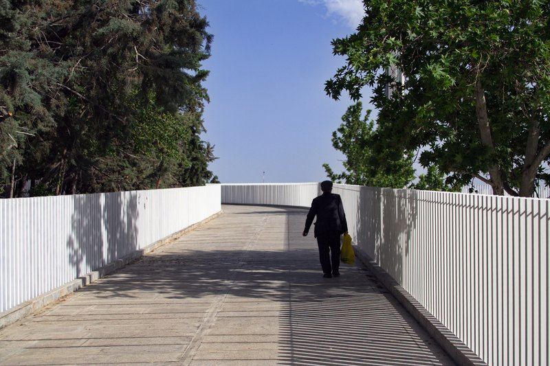 Person walking along the timber-planked pedestrian bridge flanked by white vertical metal screens