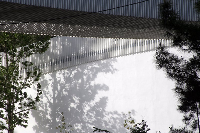 Tree shadow patterns cast across the white vertical screen wall with slatted canopy overhead