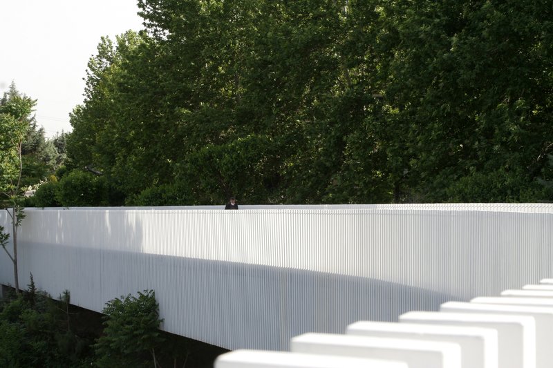 White vertical slat barrier backed by dense foliage with dappled shadows falling across its surface