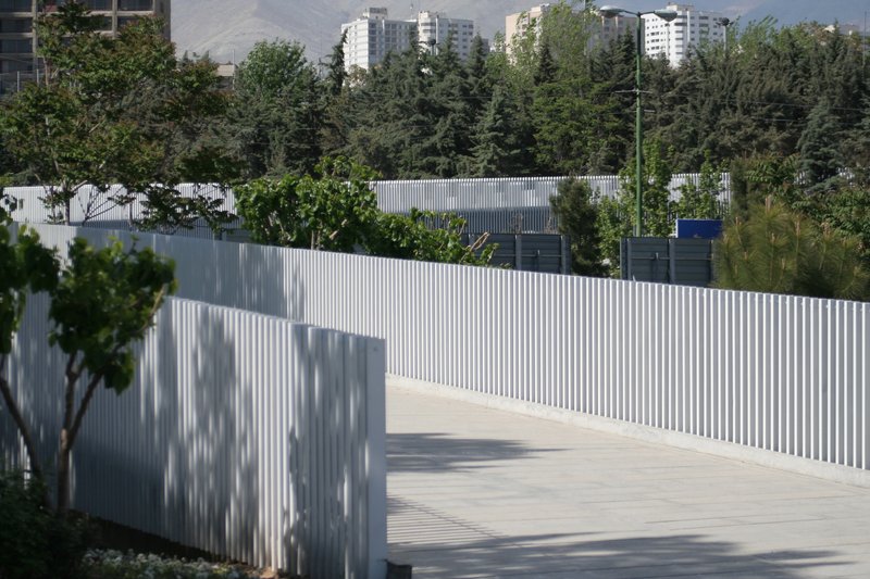 Pedestrian walkway bordered by white vertical slat railing with tree shadows cast on its surface
