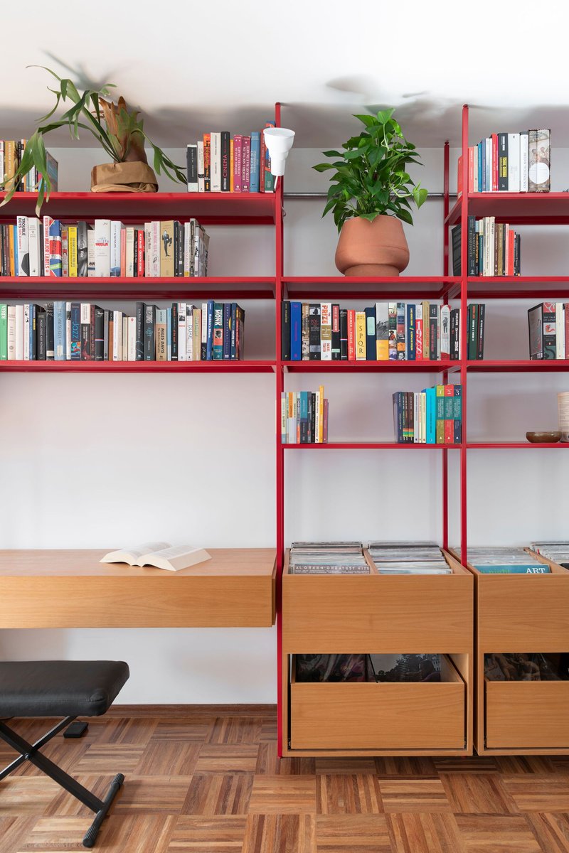 Red steel shelving unit with timber drawers below and potted plants among books
