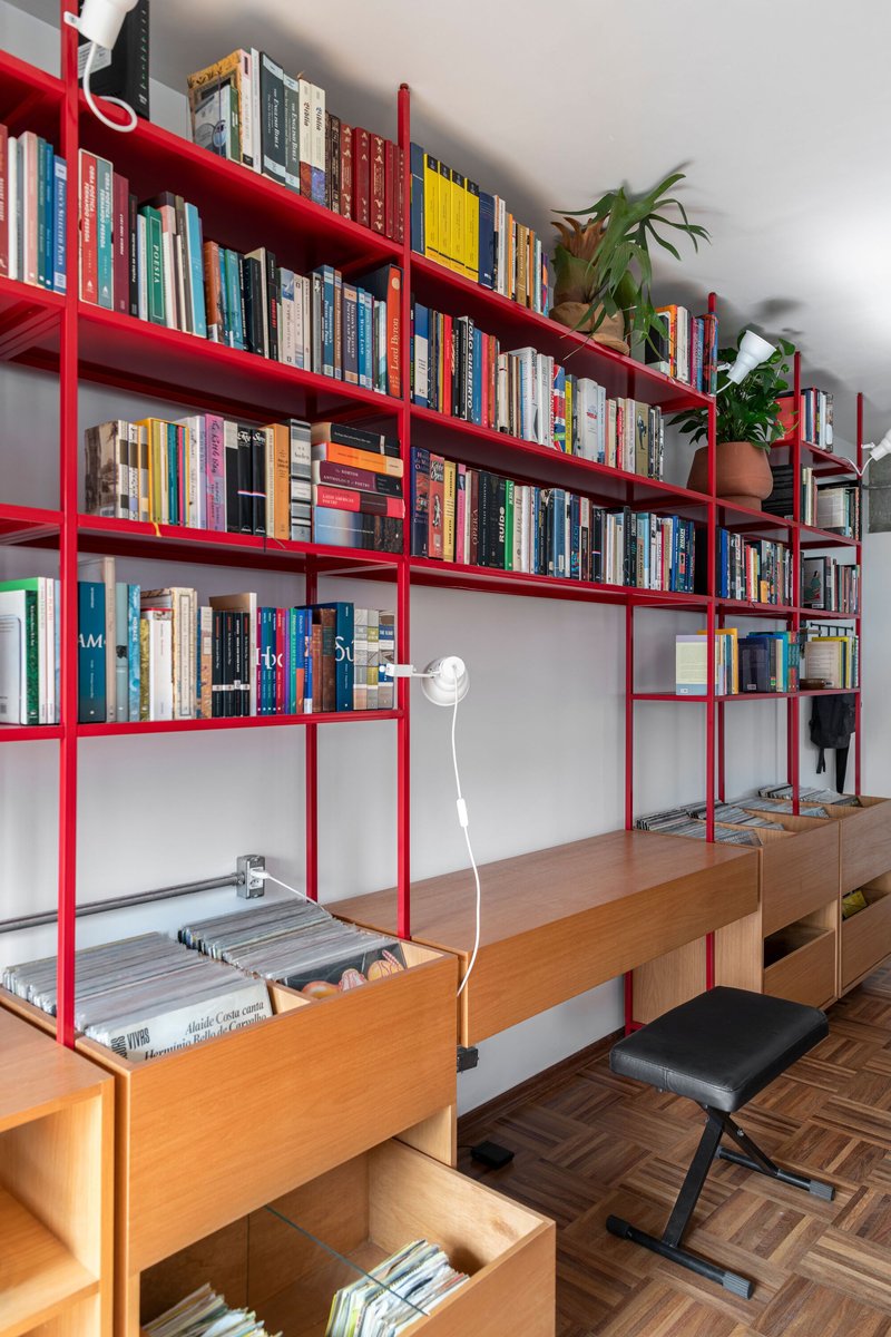 Red steel shelving system holding books and timber storage boxes on herringbone wood floor