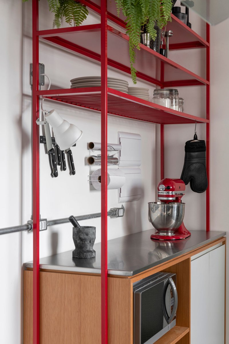 Red steel shelving frame in kitchen area with hanging knives and countertop mixer
