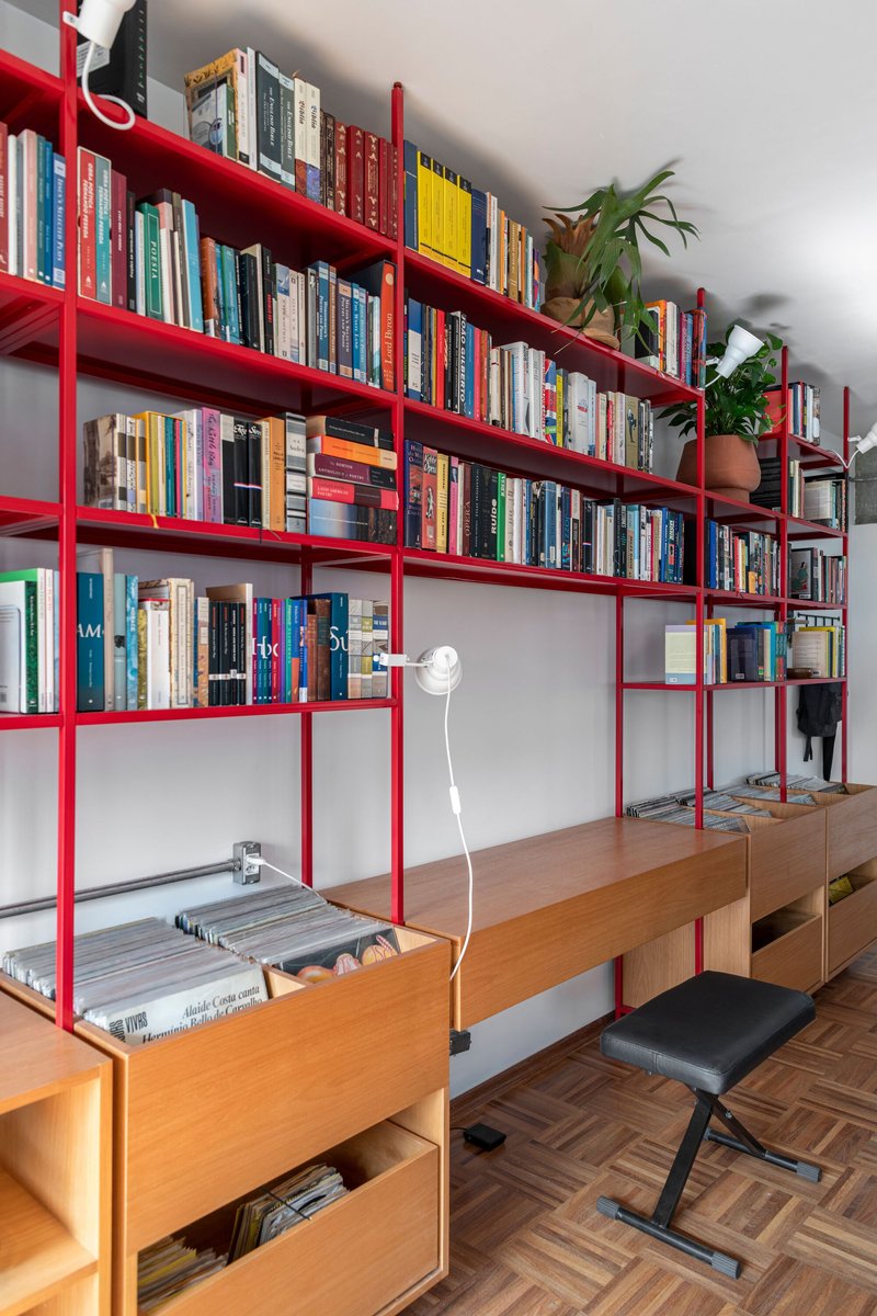Red metal shelving with timber base cabinets holding books, vinyl records and potted plants