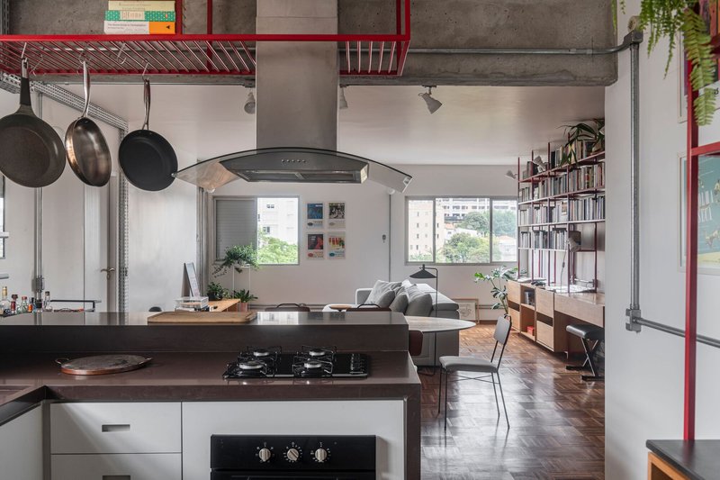 Open kitchen with island cooktop and overhead range hood facing living room with exposed concrete ceiling