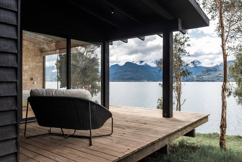 Covered timber deck with black columns and exposed beams overlooking a lake and distant mountains