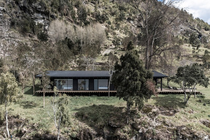 Elevated single-story volume with dark cladding and timber deck set into a sloping hillside