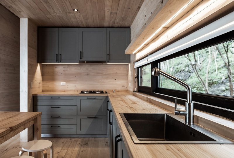 Kitchen with timber countertops, dark grey cabinetry and wood ceiling with view to forested hillside